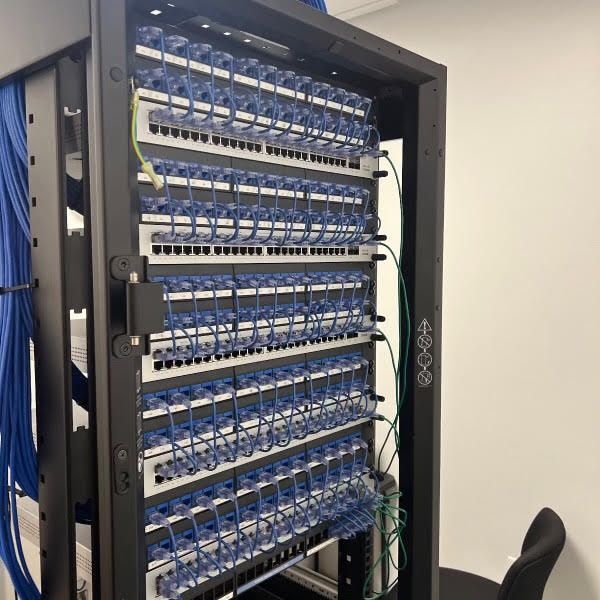 Rear of a four-post rack showing bundled blue patch cords laced to vertical cable managers.
